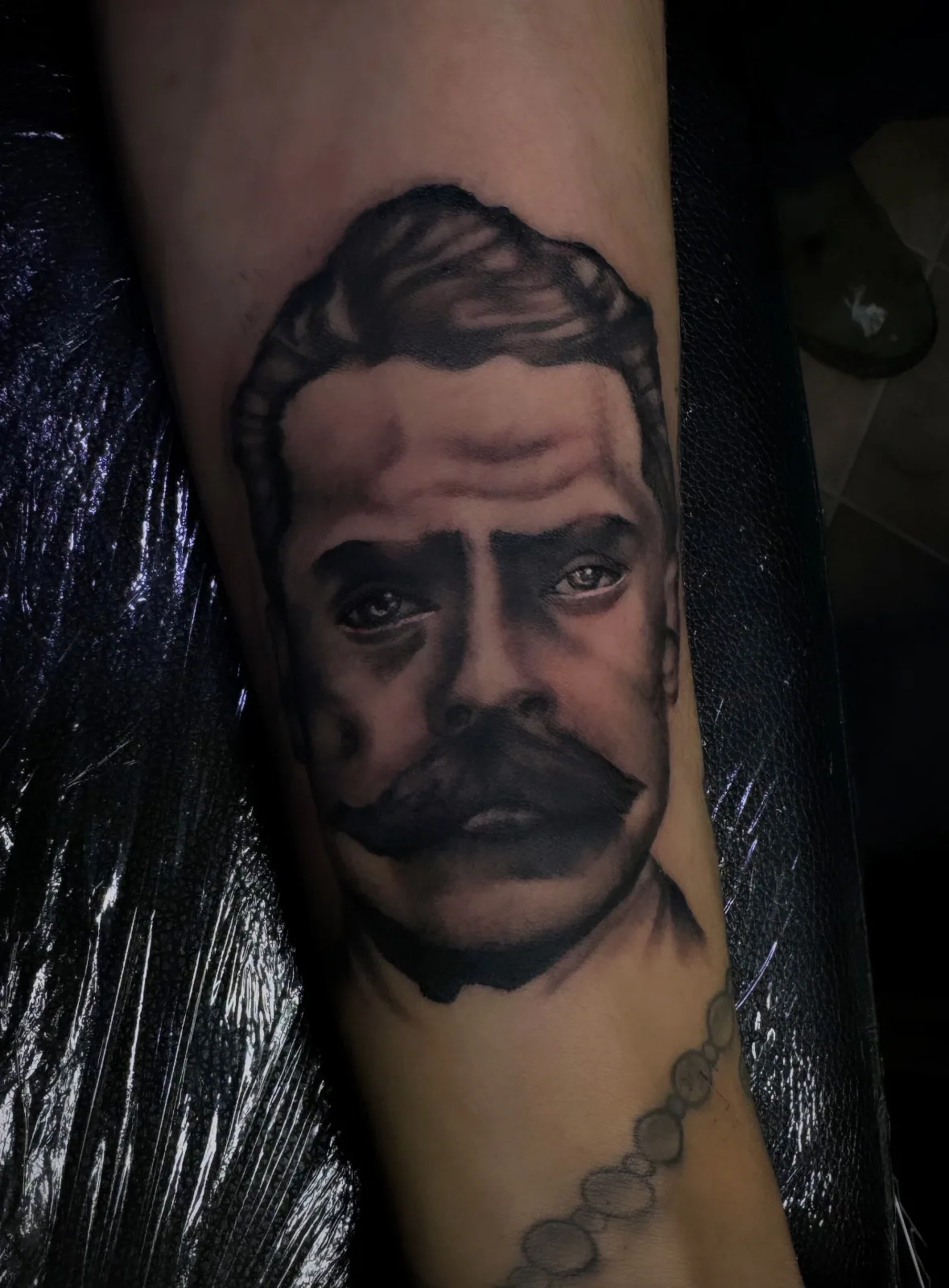 Black-and-grey Chicano-tradition portrait of a mustached revolutionary on the forearm.