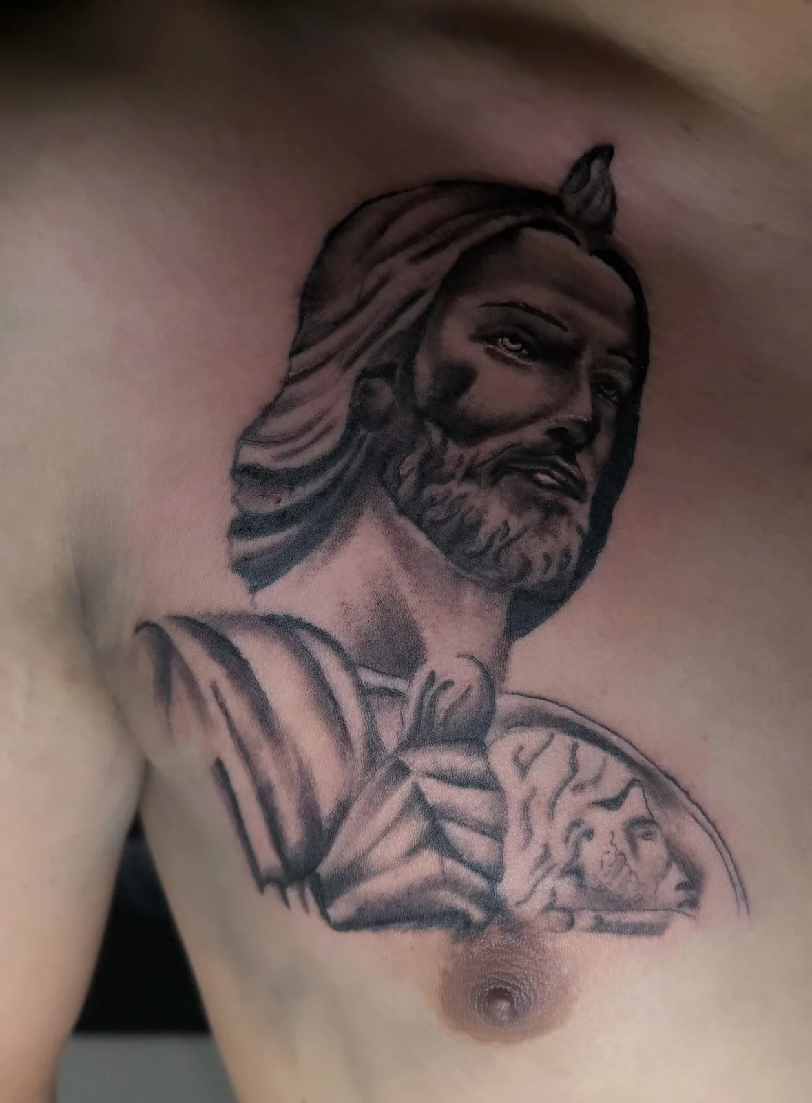 Black-and-grey realism chest tattoo of Jesus holding a lamb with flowing robes.