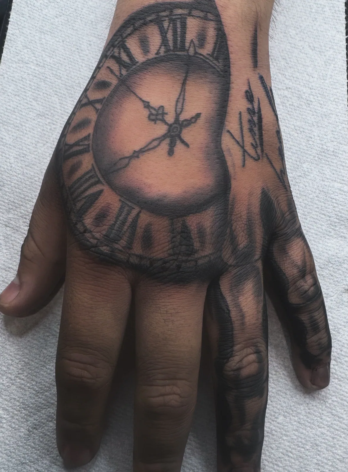 Black-and-grey realism cracked pocket watch tattoo across the back of the hand.