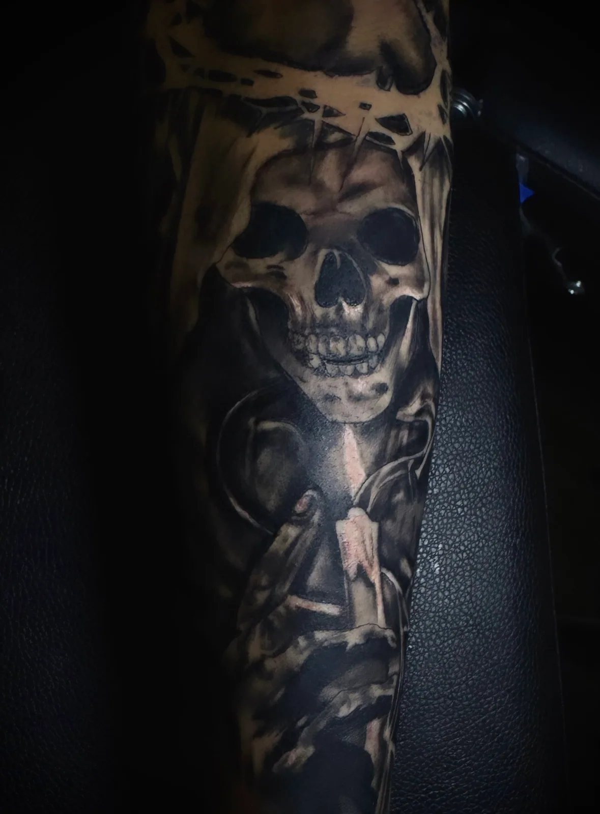 Black-and-grey realism skull tattoo wearing a crown of thorns on the upper arm.