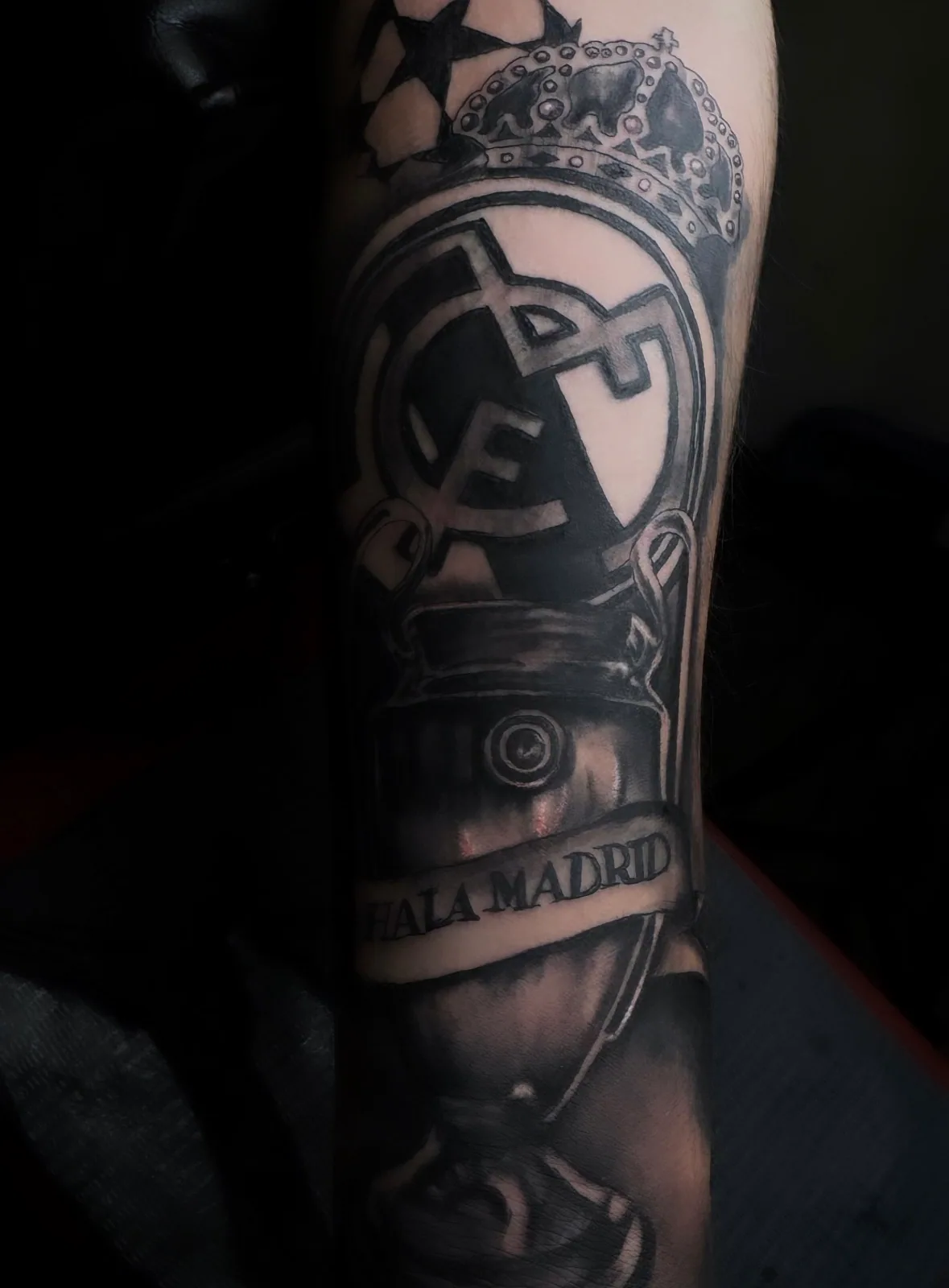 Black-and-grey forearm tattoo of the Real Madrid crest with trophy and Hala Madrid banner.