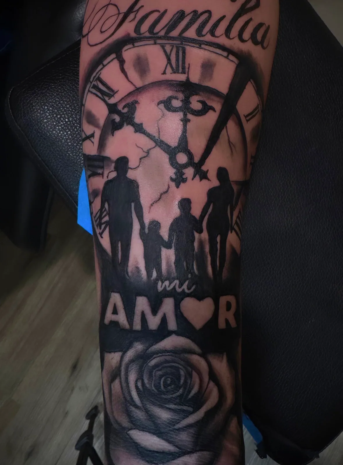 Black-and-grey Chicano-style sleeve with Familia script, family silhouettes, clock, and rose.