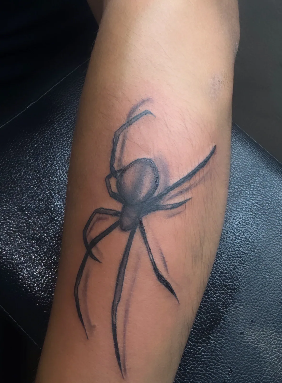 Black-and-grey realism spider tattoo with soft shading on the forearm.