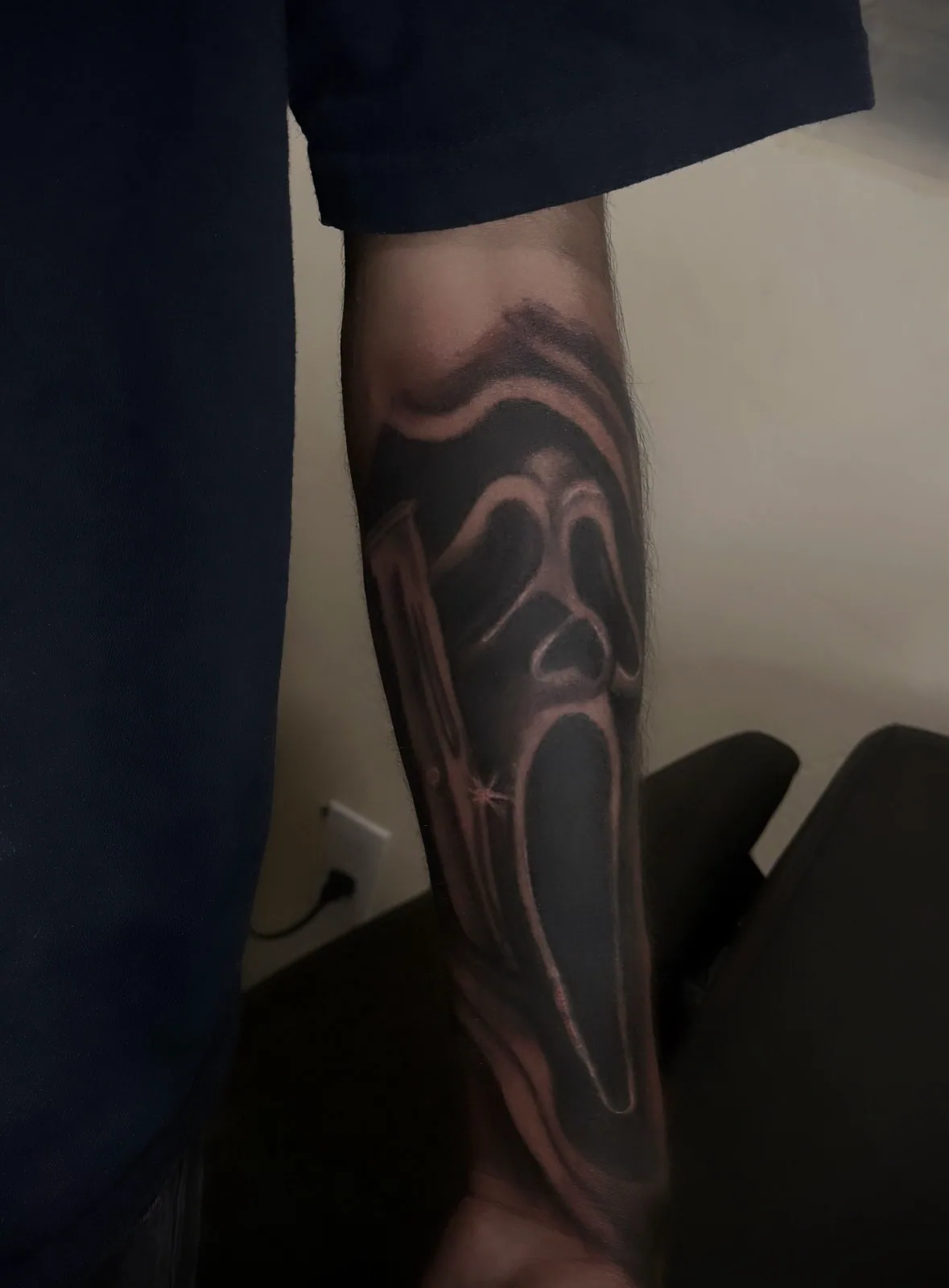 Black-and-grey realism Ghostface mask tattoo with knife on the forearm.