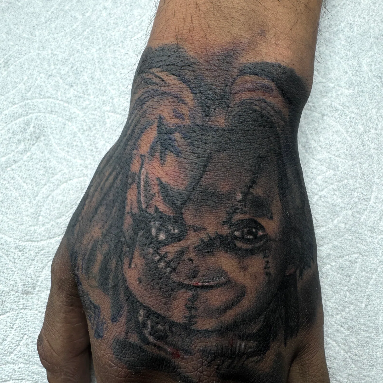 Black-and-grey realism horror portrait tattoo across the back of the hand.