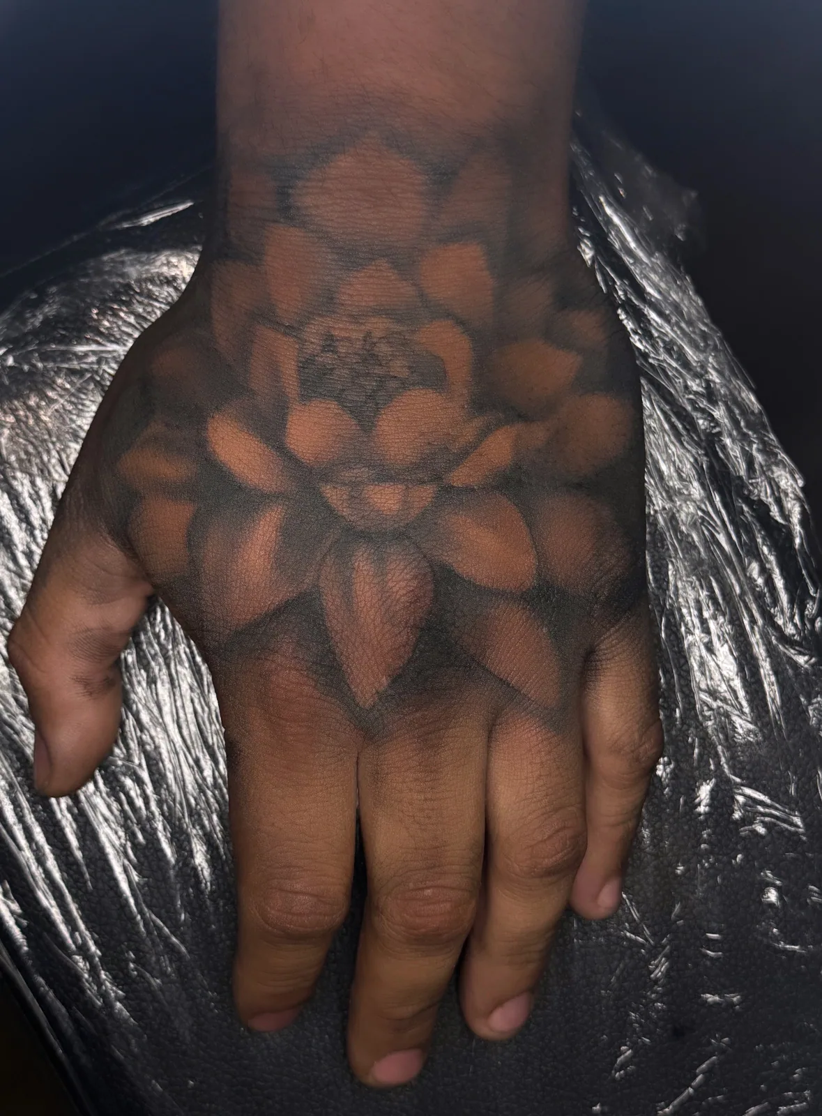 Fine-line black-and-grey lotus mandala tattoo across the back of the hand.