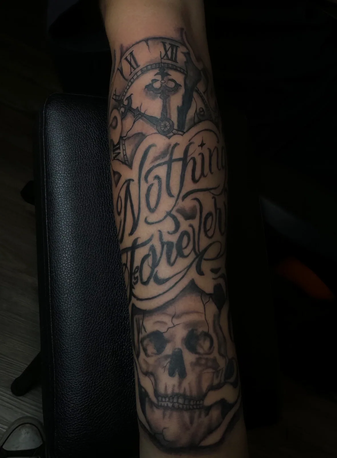 Black-and-grey forearm sleeve with Nothing is Forever script, broken clock, and skull.
