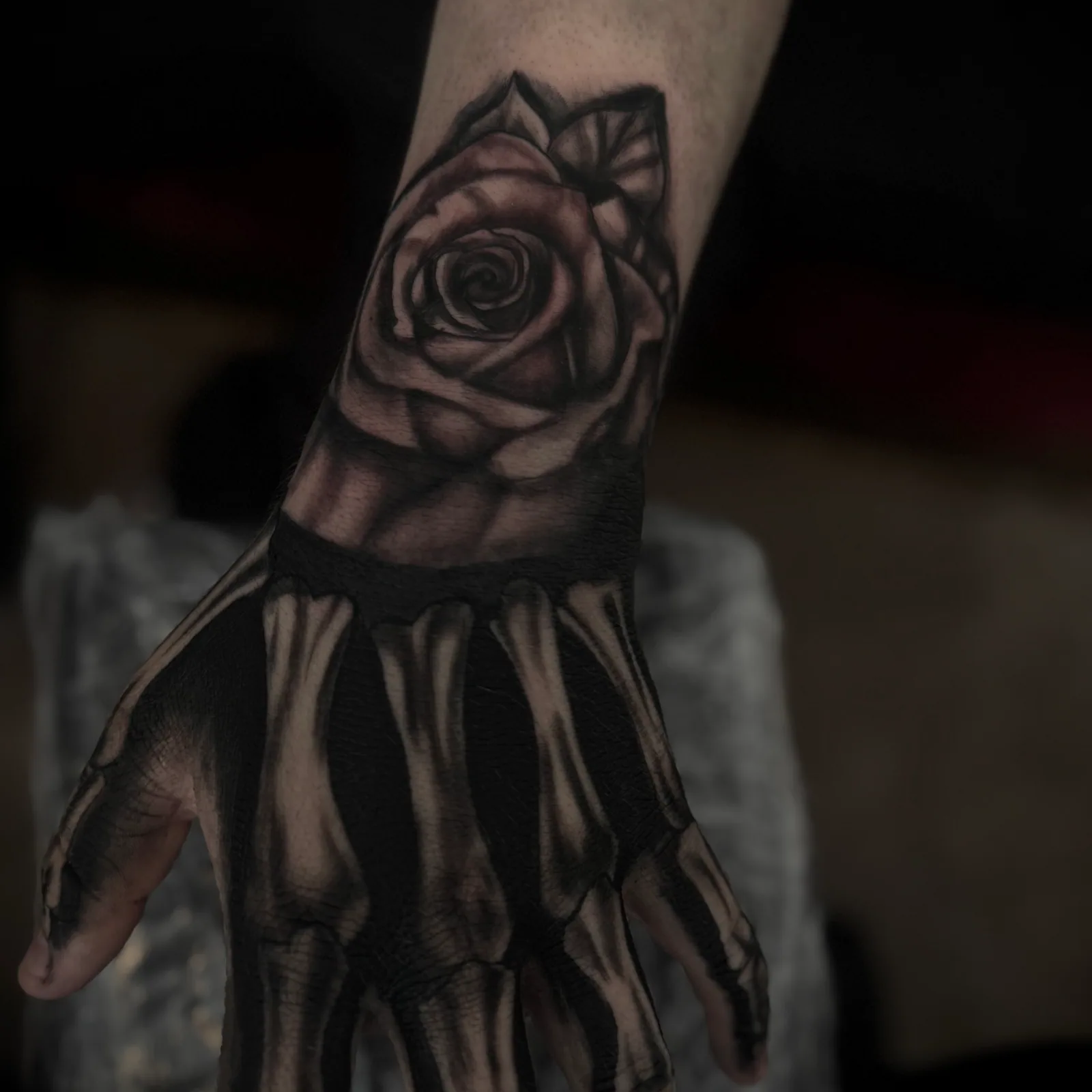 Black-and-grey realism rose tattoo flowing into a skeletal hand on the wrist and hand.